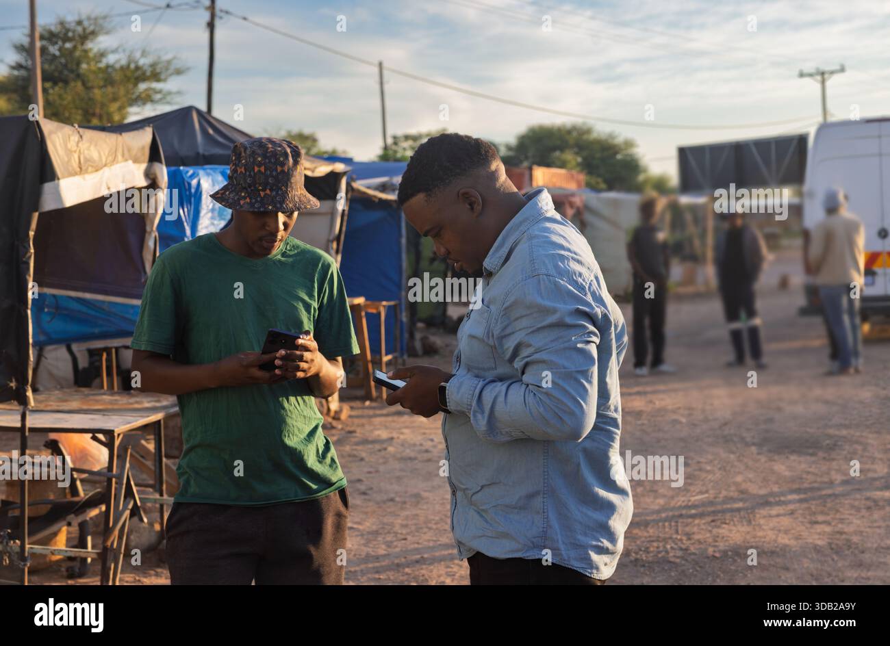 Zwei junge afrikanische Männer benutzen ein Telefon in der Altstadt am Bahnhofshandel bei Sonnenaufgang, Johannesburg, Südafrika, legere Kleidung Stockfoto