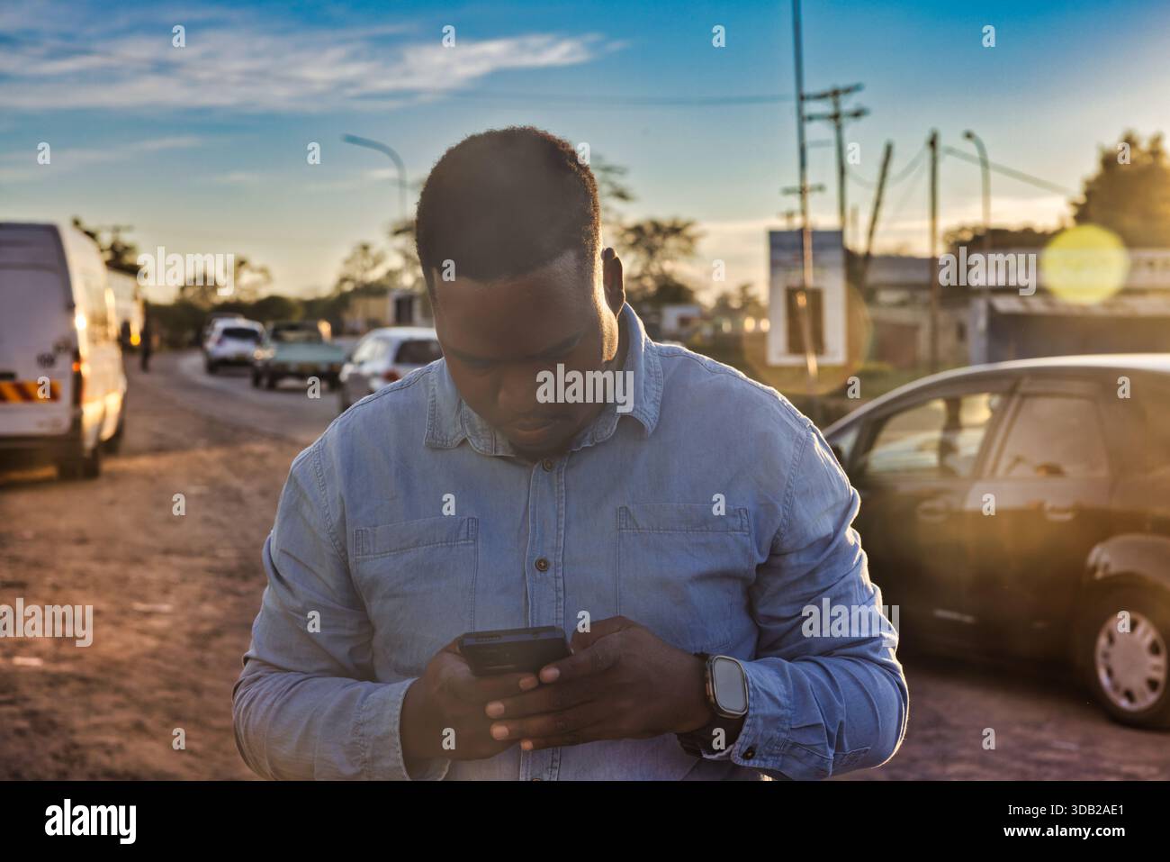 Einzelne junge afrikanische Männer benutzen ein Telefon in der Altstadt am Bahnhofshandel bei Sonnenaufgang, Johannesburg, Südafrika, Freizeitkleidung Stockfoto