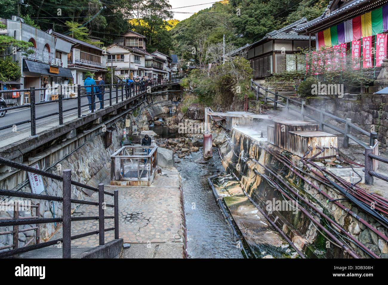 Dampf steigt aus den Steinbecken des Yuzutsu, dem öffentlichen Kochbereich im Zentrum von Yunomine Onsen, Tanabe, Präfektur Wakayama, Japan. Besucher kochen hier seit Generationen Eier und Gemüse im heißen Quellwasser. Das etwa 1.800 Jahre alte Dorf ist Teil des UNESCO-Weltkulturerbes Kumano Kodo; das Gebäude im Hintergrund ist der Yunomine-oji-Schrein mit seinen farbenfrohen Vorhängen. Stockfoto