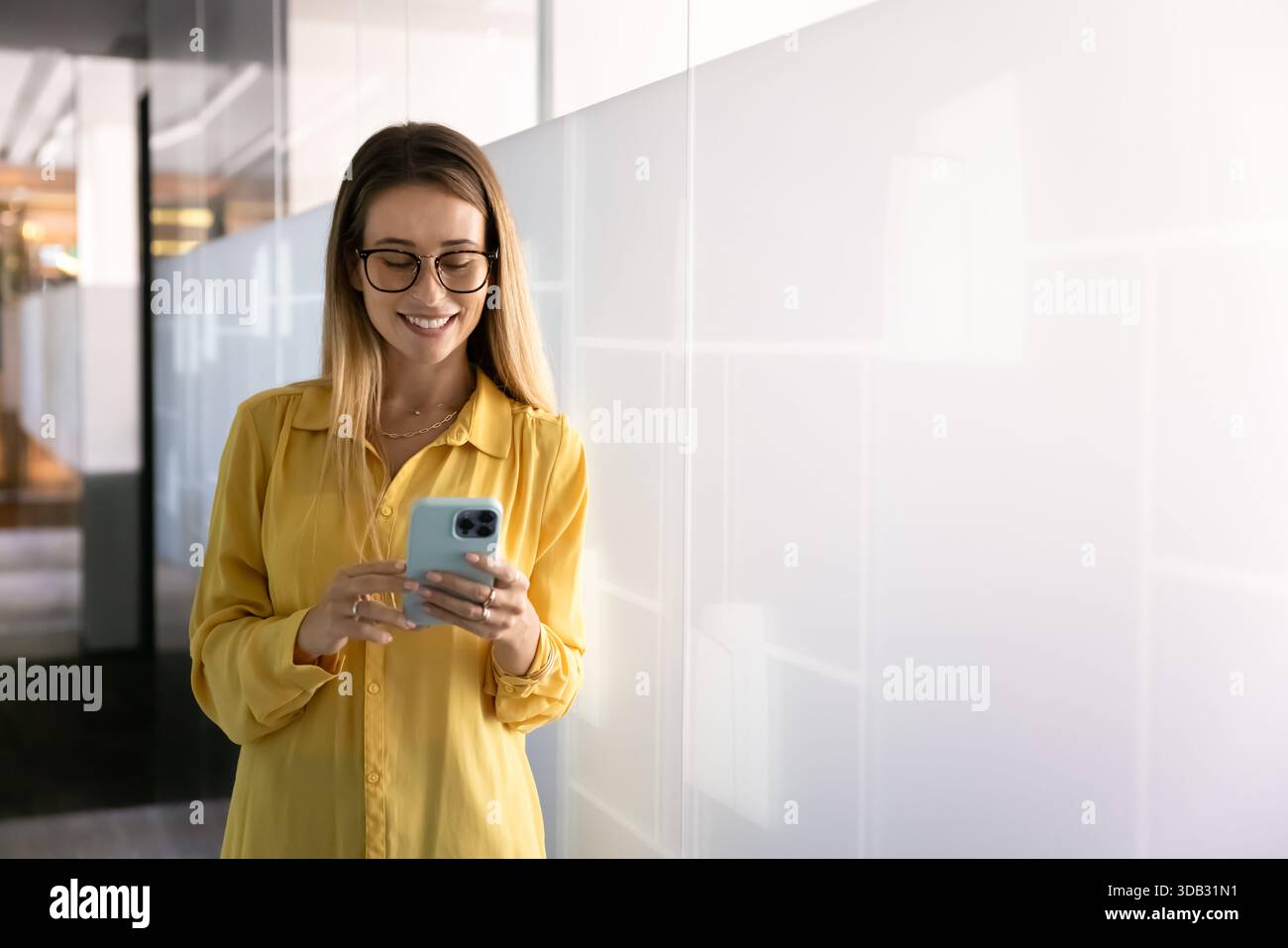 Positive, stilvolle junge professionelle Frau mit Brille, die auf dem Smartphone schreibt Stockfoto