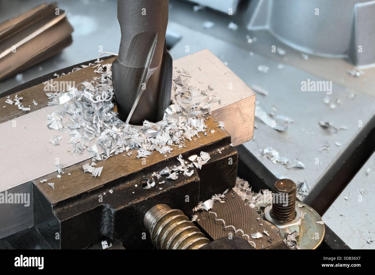 Vollkernbohrer vergrößern das Loch in Aluminiumprofil und Metallspänen. Großaufnahme scharfes Stahlschneidewerkzeug bei der Arbeit in Werkstück, das in einen Schraubstock gespannt ist. Stockfoto