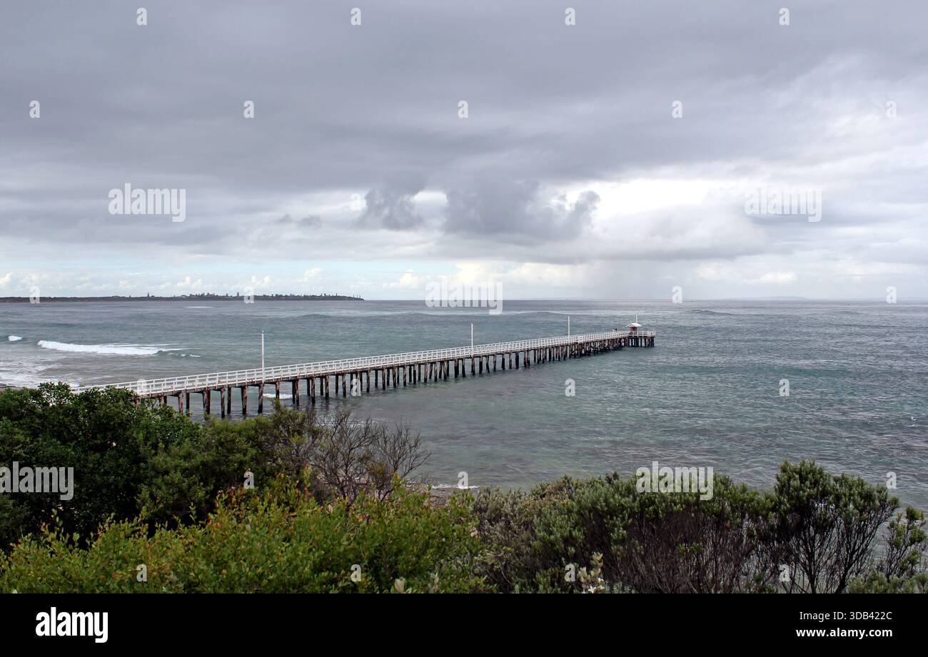Hölzerner Pier, der sich in einen Ozean unter einem bewölkten stürmischen Himmel am Point Lonsdale in Victoria, Australien, erstreckt Stockfoto