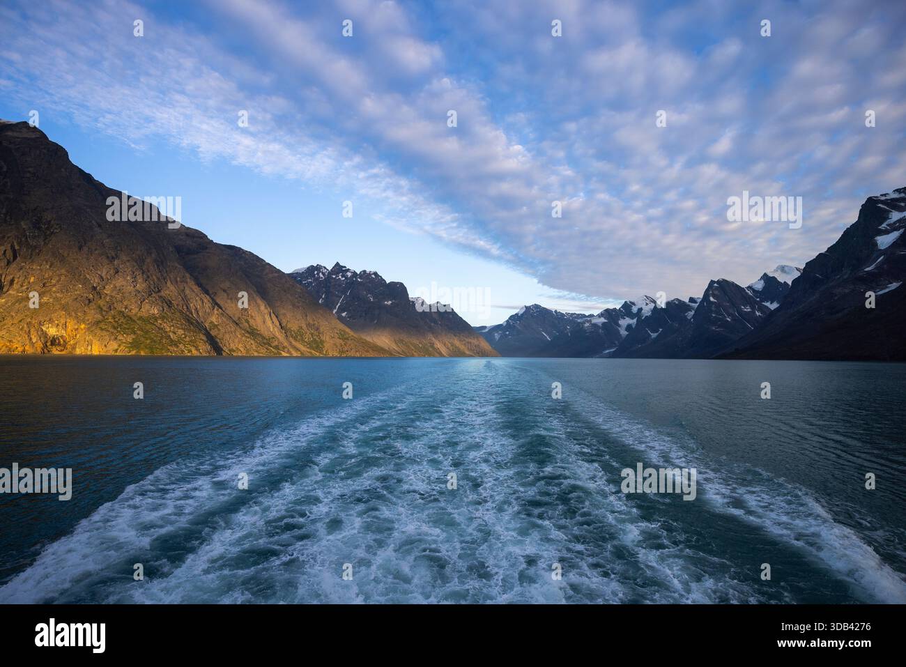 Winken Sie hinter dem Kiel des Expeditionskreuzfahrtschiffes World Voyager (Atlas Ocean Voyages) mit Bergen bei Sonnenuntergang, in der Nähe des Evighedsfjorden (Eternity Fjord) Stockfoto