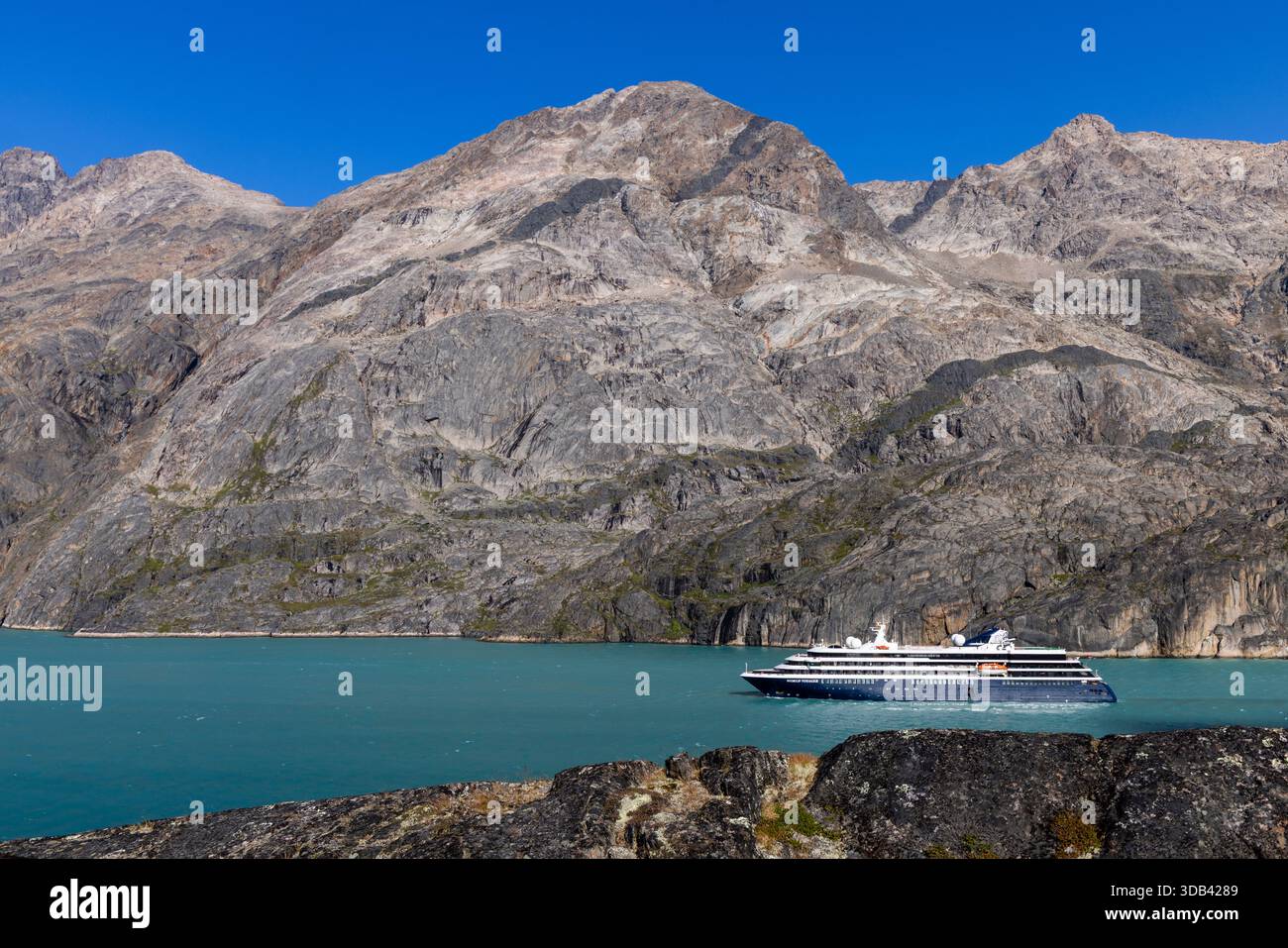 Expeditionskreuzschiff World Voyager (Atlas Ocean Voyages) mit Felsen im Vordergrund und Bergen dahinter, Sermillinnguaq Fjord, Queqatta, Greenlan Stockfoto