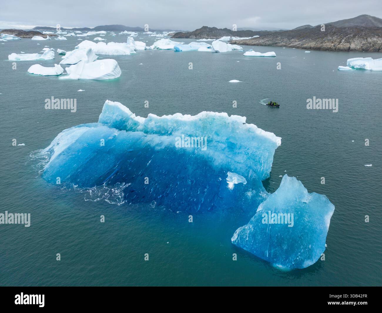 Aus der Vogelperspektive eines aufblasbaren Zodiac-Bootes vom Expeditionskreuzschiff World Voyager (Atlas Ocean Voyages) hinter einem blauen Eisberg, Neria Fjord, Sermer Stockfoto