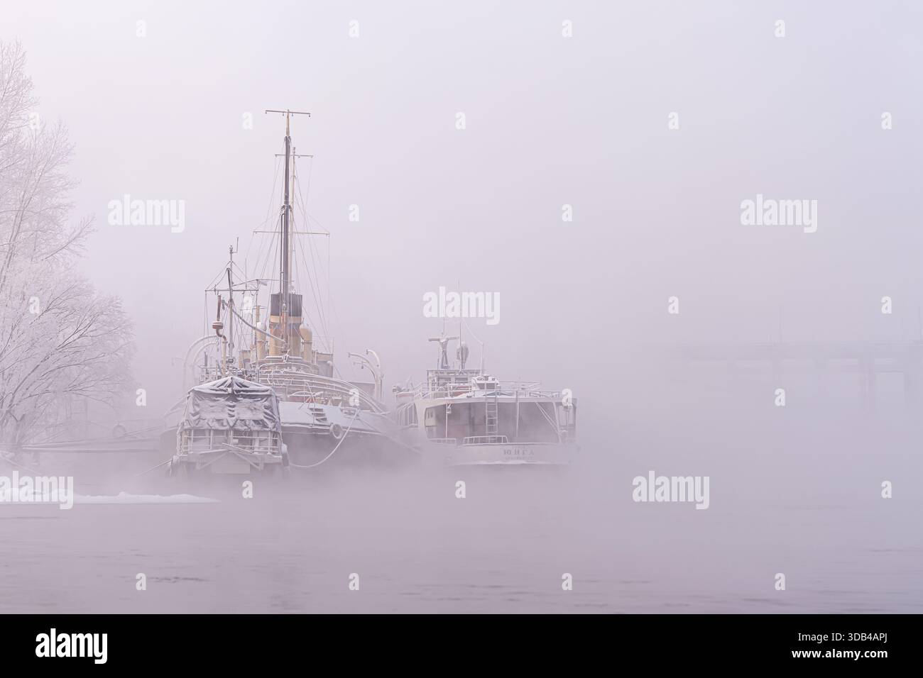 Atmosphärische Nebellandschaft mit nostalgischer Stimmung. Alte stillgelegte Schiffe, eine Jung-Straßenbahn und ein Schlepper oder ein Fluss-Eisbrecher permanent geparkt Stockfoto