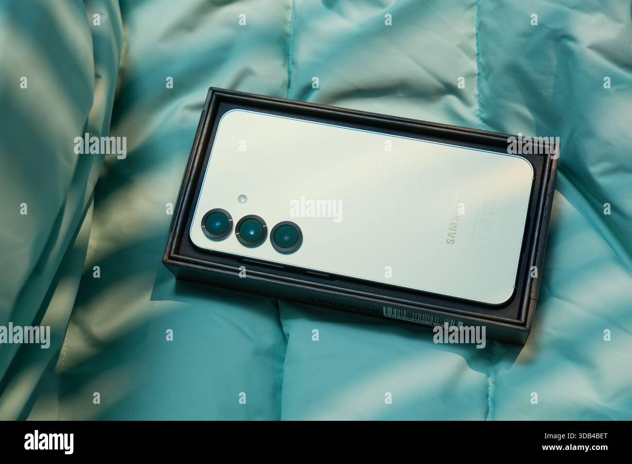 Tyumen, Russland-11. Dezember 2025: Ein Smartphone liegt in seiner Box auf einer weichen, strukturierten Oberfläche. Das Gerät zeigt seine Rückseite mit mehreren Kameraobjektiven Stockfoto