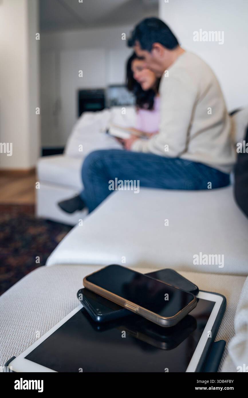 Selektiver Fokus auf Smartphones mit verschwommenem Paar, das im Hintergrund ein Buch liest. Konzept der digitalen Detox und Wahl der analogen statt der Technik. Stockfoto