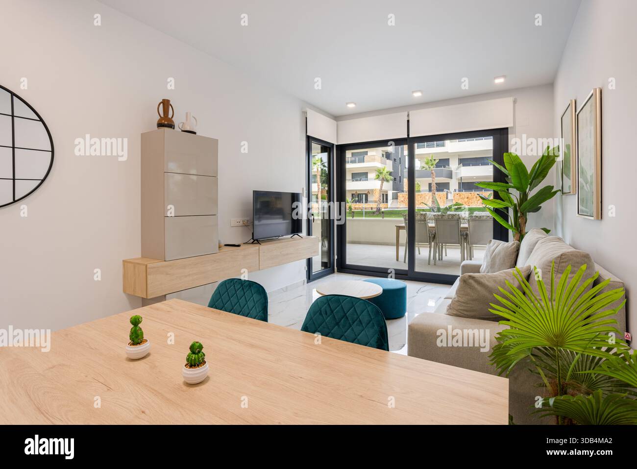 Heller Wohnbereich des Apartments mit blauen Stühlen, Holzmöbeln, Pflanzen und Zugang zur Terrasse Stockfoto