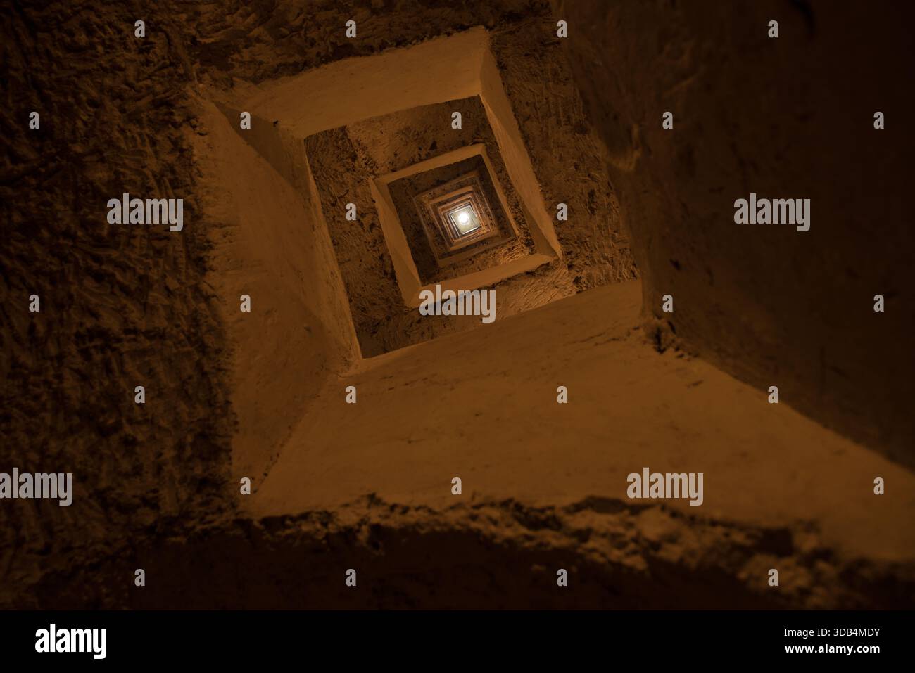 Square Lightwell Lookup – warmer, strukturierter Steinschaft mit konzentrischen Quadraten und dramatischer vertikaler Perspektive Stockfoto