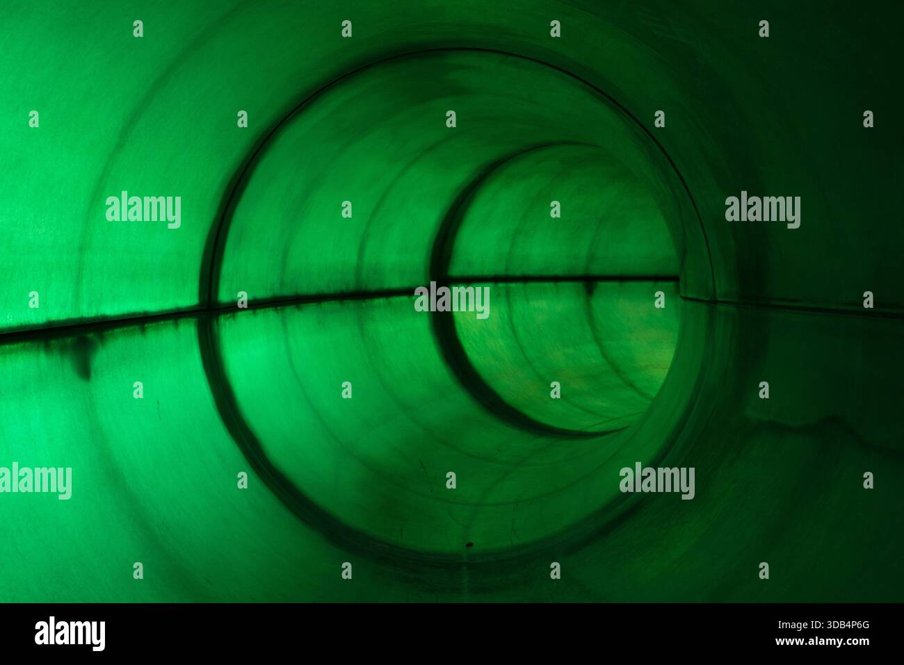 Grün beleuchtete runde Wasserrutsche innen mit symmetrischer Spiegelreflexion Stockfoto