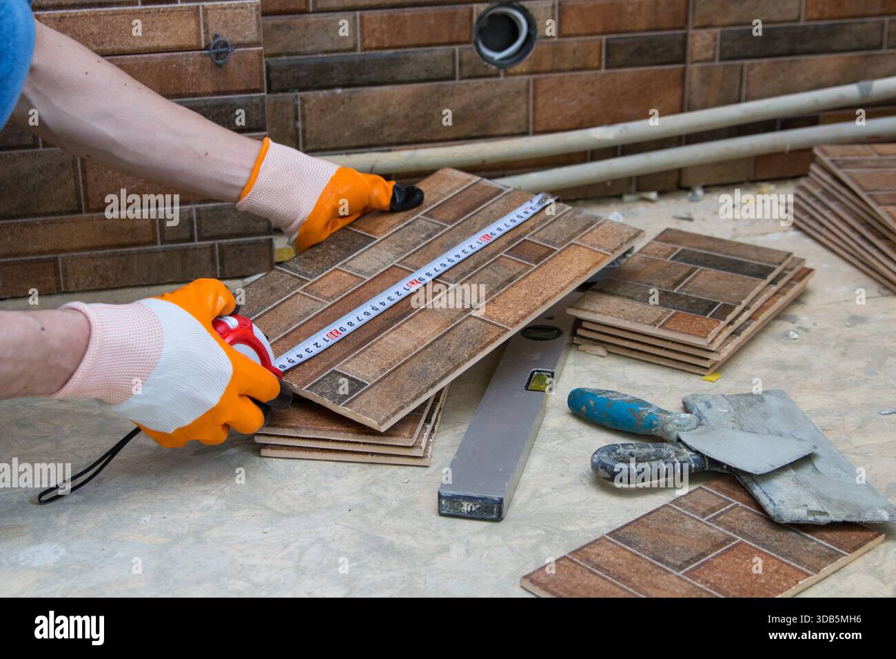 Ein Mann misst eine Keramikfliese mit einem Maßband zum Schneiden Stockfoto