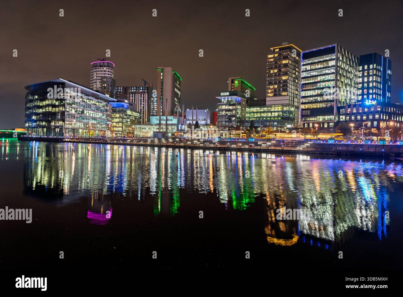Salford Quays Medienstadt bei Nacht. Der BBC-Studiokomplex spiegelt sich auf dem Dock von Pomona wider. Stockfoto