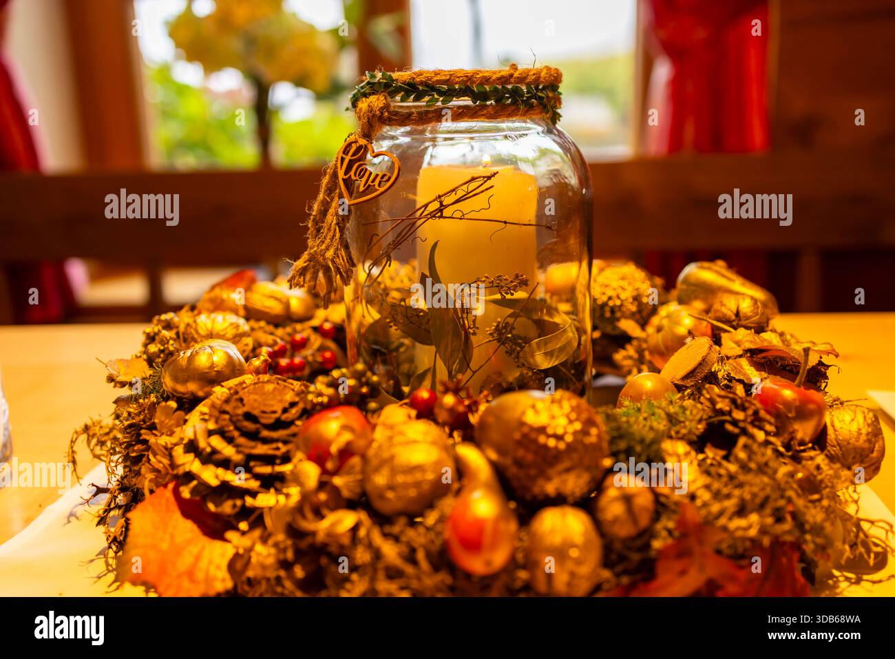 Herbstlicher Tisch im Mittelpunkt mit einer leuchtenden Kerze in einem dekorativen Glas, umgeben von natürlichen Elementen Stockfoto