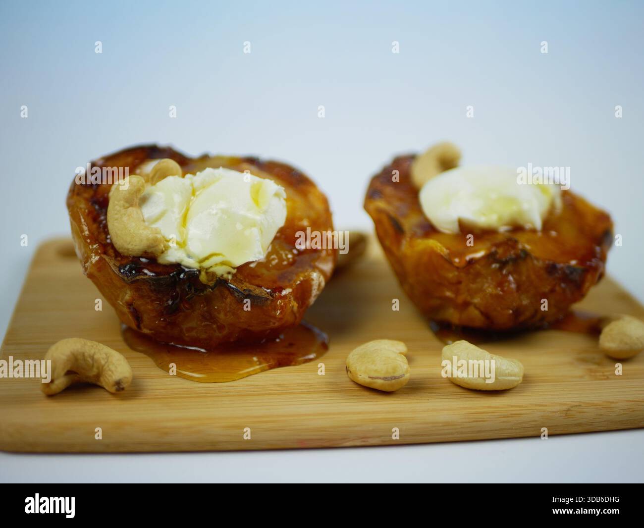 Gebackene Apfelhälften mit Frischkäse, Honig und Cashewnüssen auf Holzbrett, letzte Portion mit gemütlichen hausgemachten Apfeldesserts für Herbstkochen, s Stockfoto
