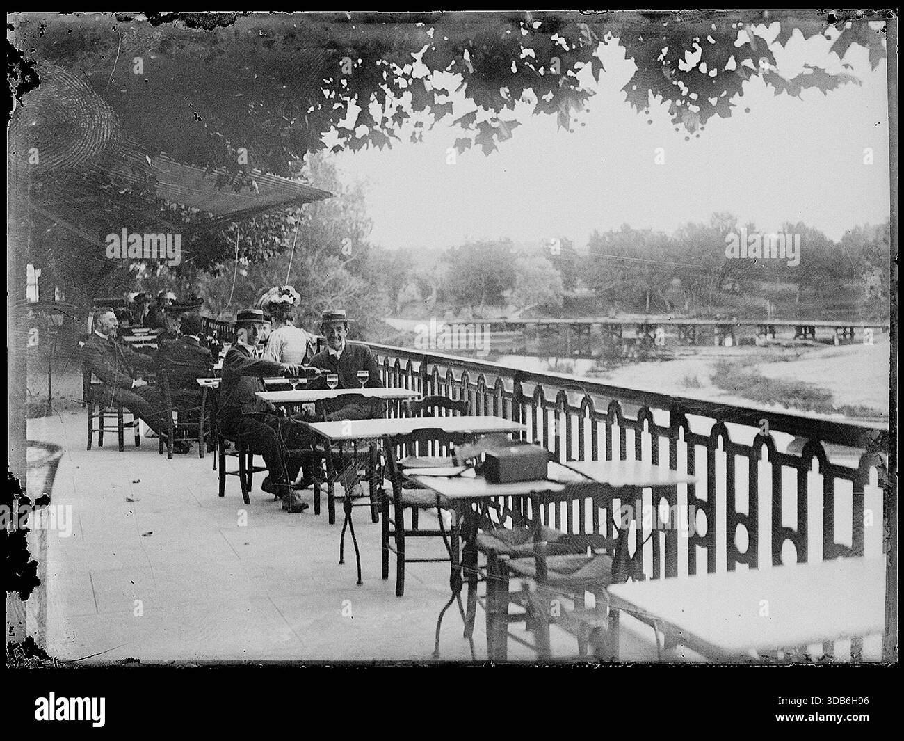 Mehrere Personen saßen auf einer Café-Terrasse mit Blick auf den Park. Anfang des 20. Jahrhunderts. - Stockfoto