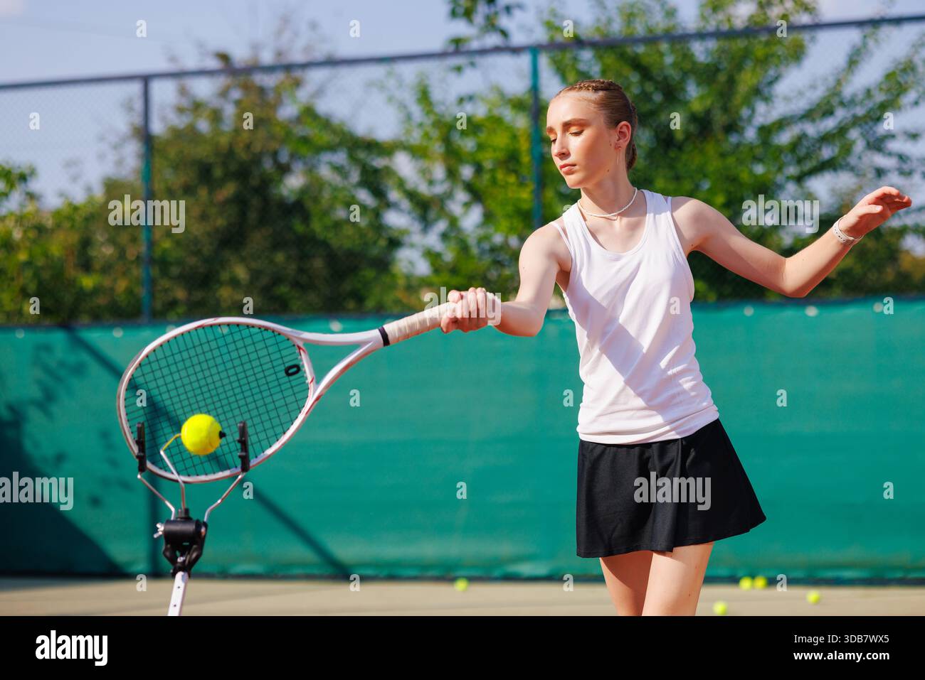 Teen Girl übt Tennis im Vorfeld mit Trainingshilfe auf dem Platz, konzentriert während des Trainings im Freien. Stockfoto