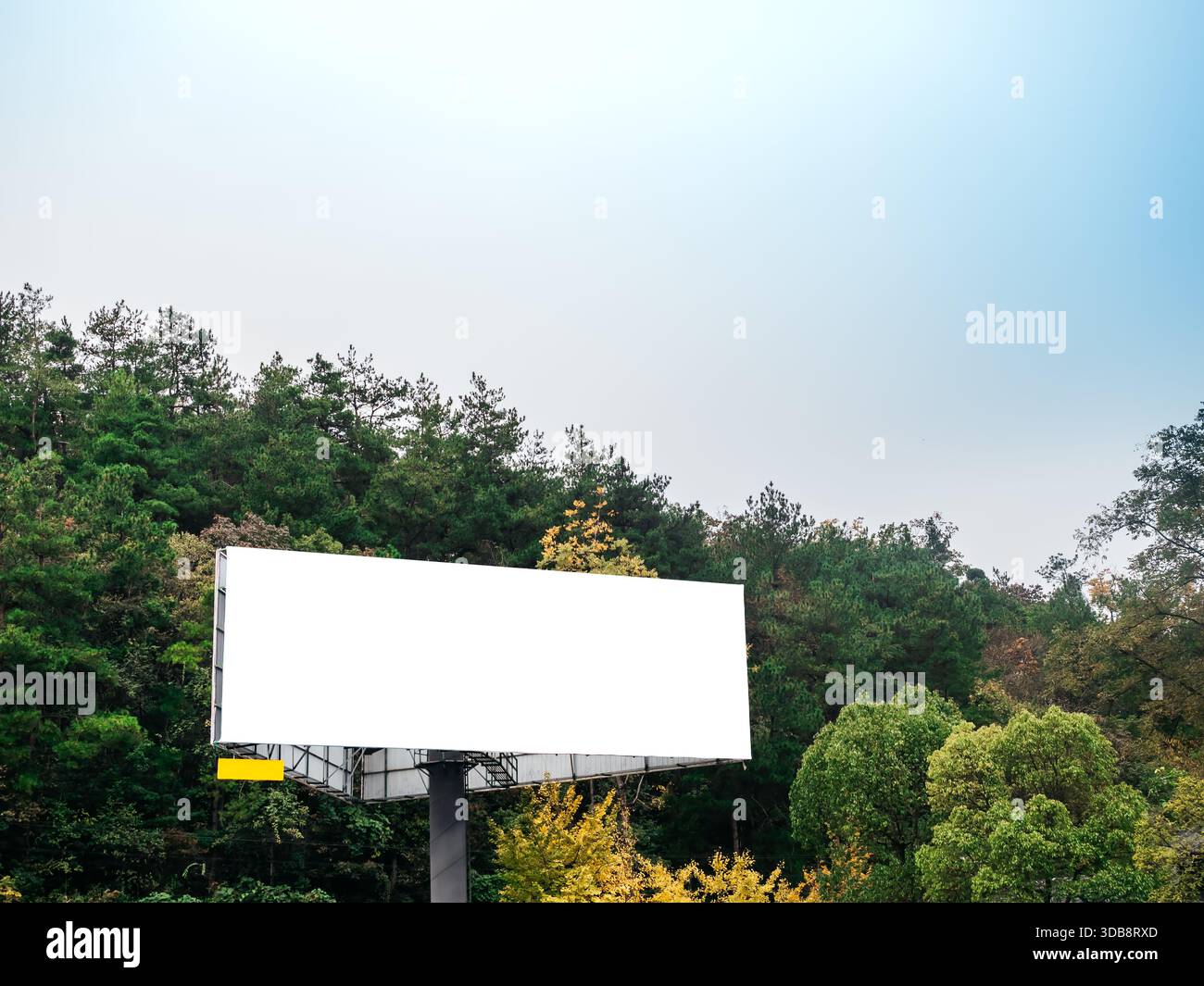 Leeres weißes Reklametafelmodell, das in der Nähe eines Berggrünen Waldes unter klarem Himmel steht, ideal für Außenwerbung, Werbekampagnen und Design-P Stockfoto