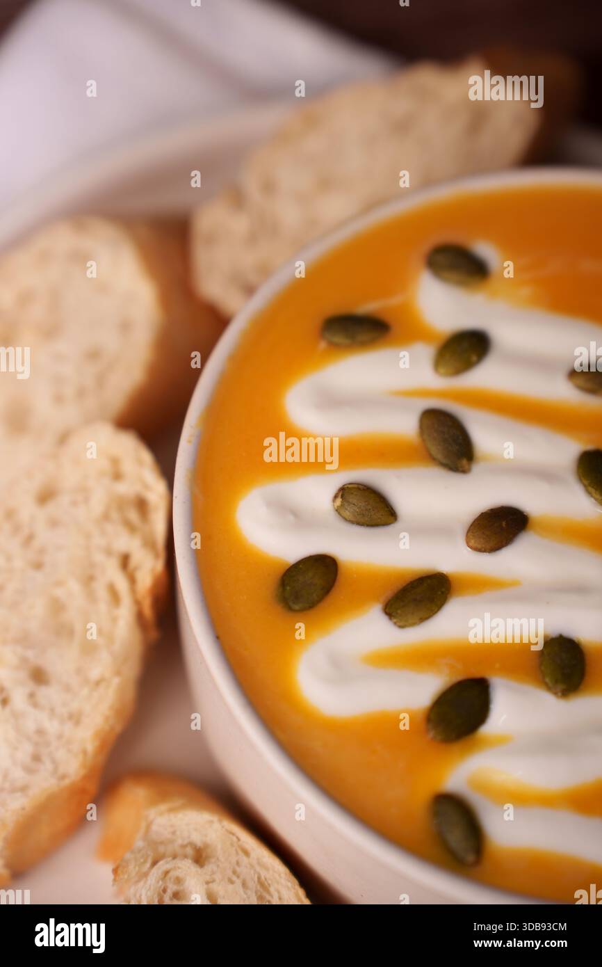 Warme Herbstsuppe mit cremigem Wirbel und pepitas in weißer Schüssel, begleitet von frischen Brotscheiben, die Komfort und saisonale Aromen mit satter Orange wecken Stockfoto