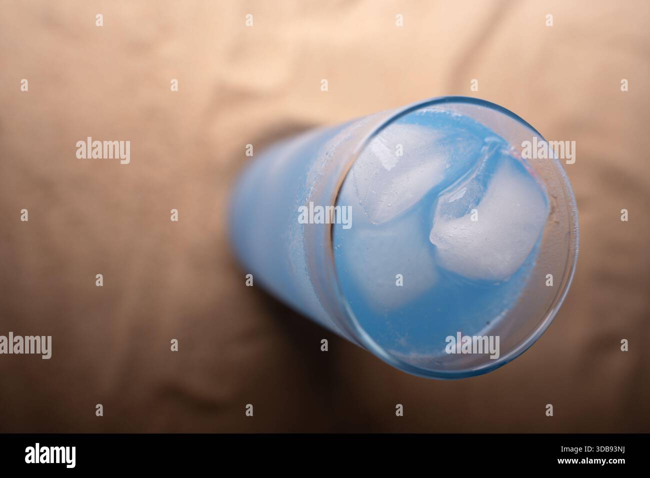 Nahaufnahme eines kühlen, erfrischenden blauen Getränks mit Eiswürfeln in einem hohen Glas auf weichem beigefarbenem Hintergrund, das kühlende Gelassenheit und minimalistisches El unterstreicht Stockfoto