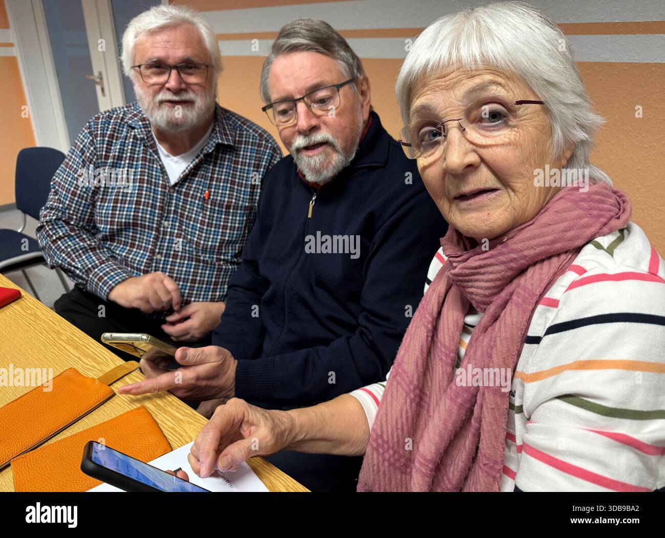 PRODUKTION - 10. Dezember 2025, Linsengericht: Der digitale Führer Peter Grimm (l) erklärt Horst und Brigitta Schallmayer, wie man eine WhatsApp-Gruppe mit Freunden aufbaut und Benachrichtigungen von Google auf ihrem Handy löscht. Beim Freiwilligenprojekt im Linsengericht geht es in erster Linie darum, Senioren Schritt für Schritt zu informieren und sie unter fachkundiger Anleitung selbst zu lösen. Foto: Michael Bauer/dpa Stockfoto