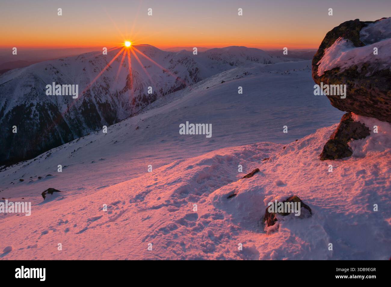 Aus der Vogelperspektive auf die Sonne, die über den schneebedeckten Gipfeln von Derese in der Niederen Tatra ragt, gebadet im warmen Schein der Morgendämmerung, Niedere Tatra, Zilina Region, Stockfoto
