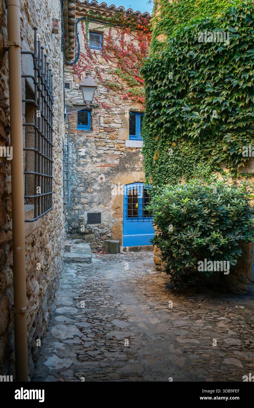 Enge Steinallee führt zu einem Gebäude mit leuchtenden blauen Fenstern und Türen in Peratallada, Katalonien, Spanien Stockfoto