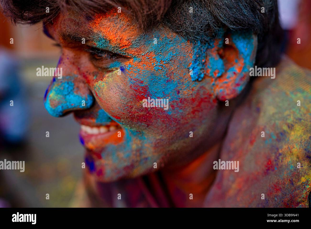 Mann lächelt mit Gesicht bedeckt mit bunten Pudern während des Holi Festivals in Indien – feiert Freude, Tradition und die lebendigen Farben der indischen Kultur. Stockfoto