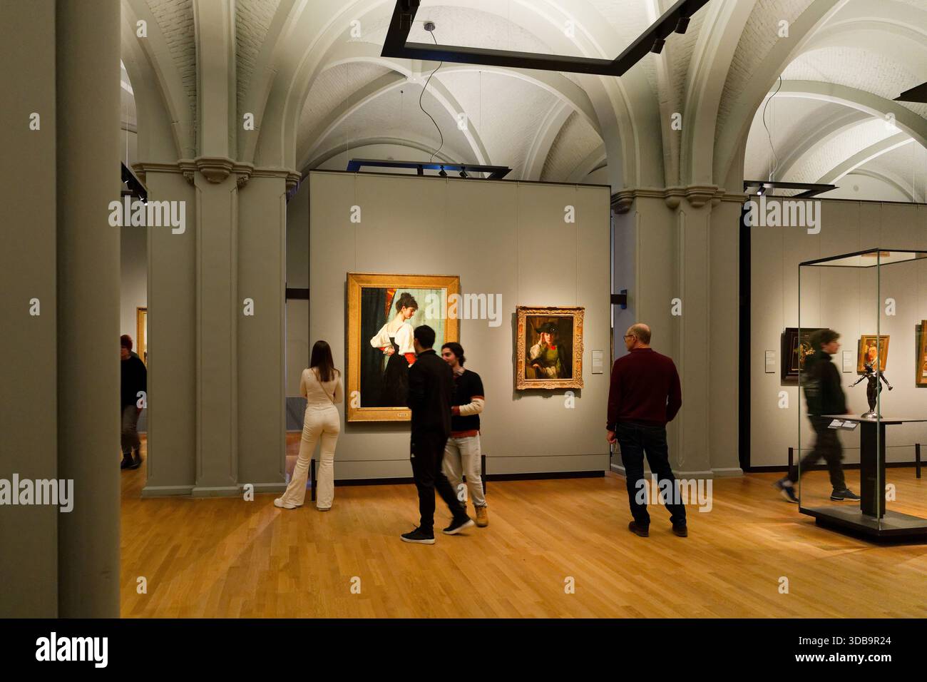 In einer zeitgenössischen Kunstgalerie mit historischen Gemälden erkunden die Menschen verschiedene Kunstwerke. Die Atmosphäre vermittelt Wertschätzung für Kultur und cr Stockfoto