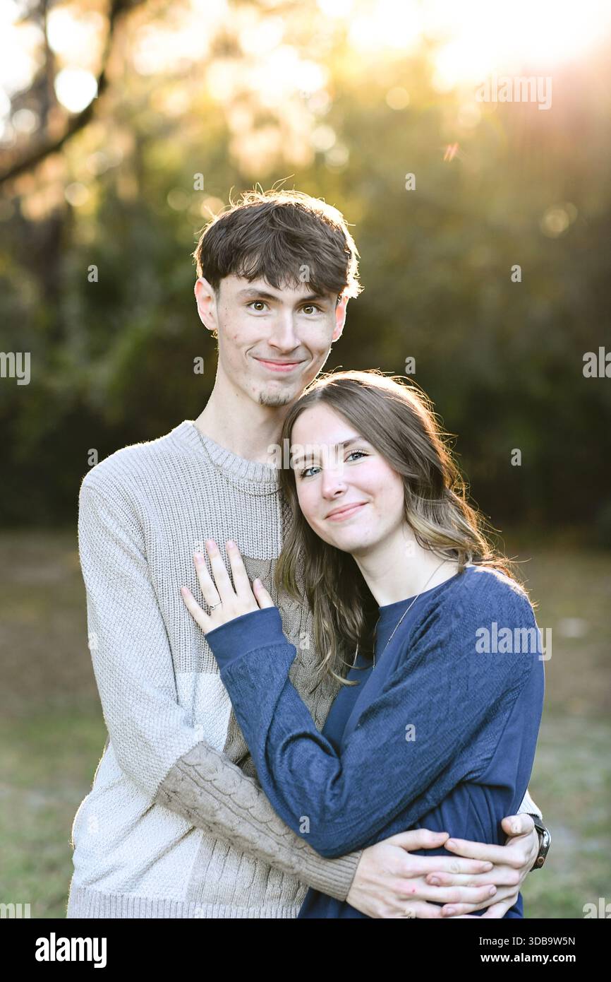 Ein junges Paar, das sich in warmem goldenem Sonnenlicht umschließt und lächelt. Stockfoto