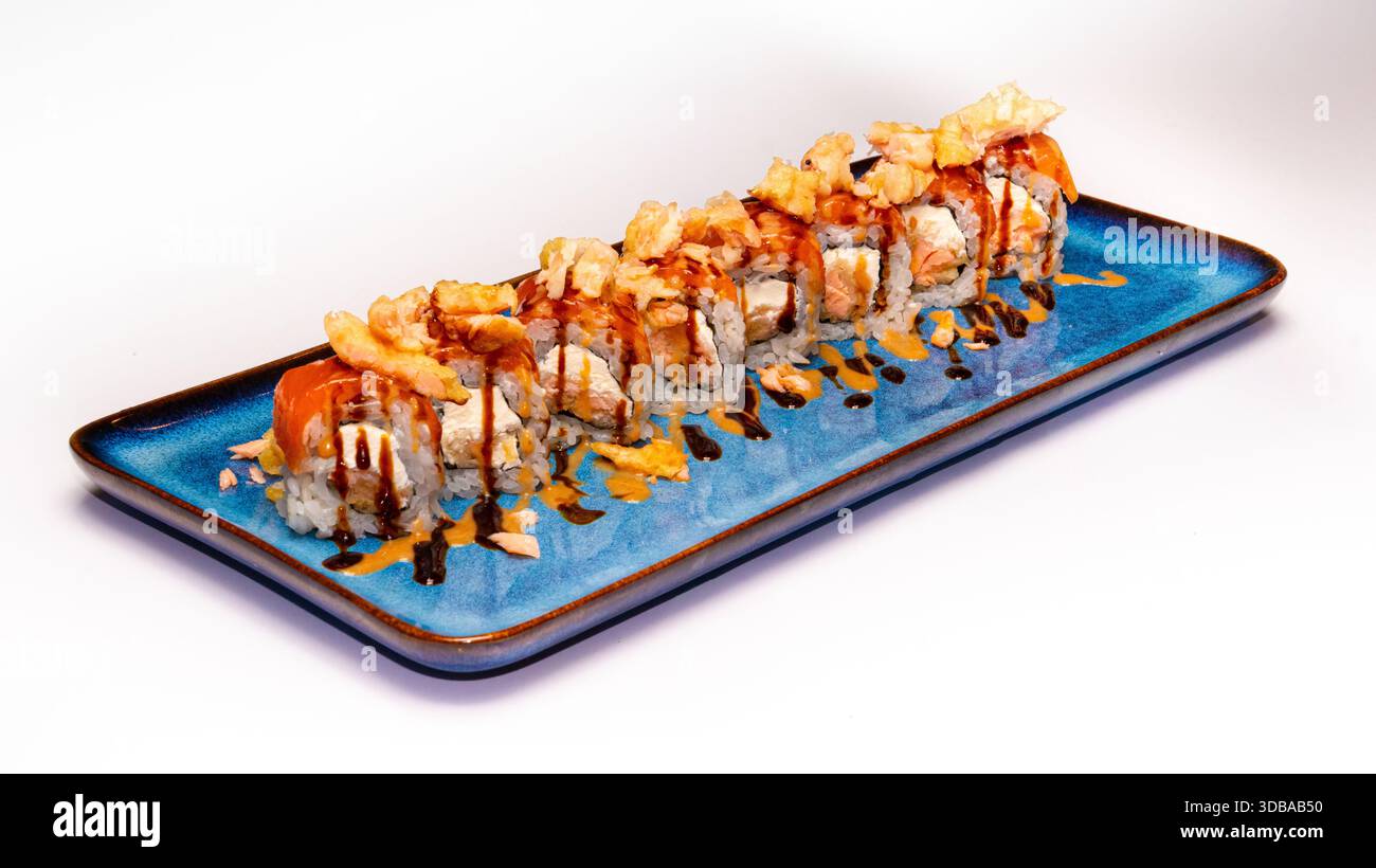 Fusion Uramaki Sushi-Brötchen mit Lachs, knusprigem Topping und Sauce Nizzle serviert auf blauer Keramikplatte isoliert auf weißem Hintergrund. Stockfoto