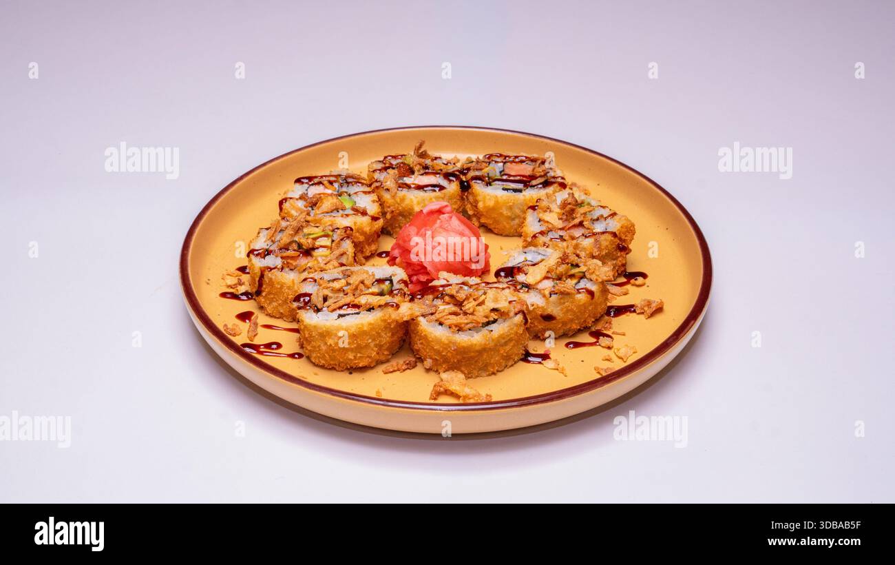 Frittierte Sushi-Brötchen mit knusprigen Zwiebeln und Sauce serviert auf gelber Keramikplatte isoliert auf weißem Hintergrund. Stockfoto