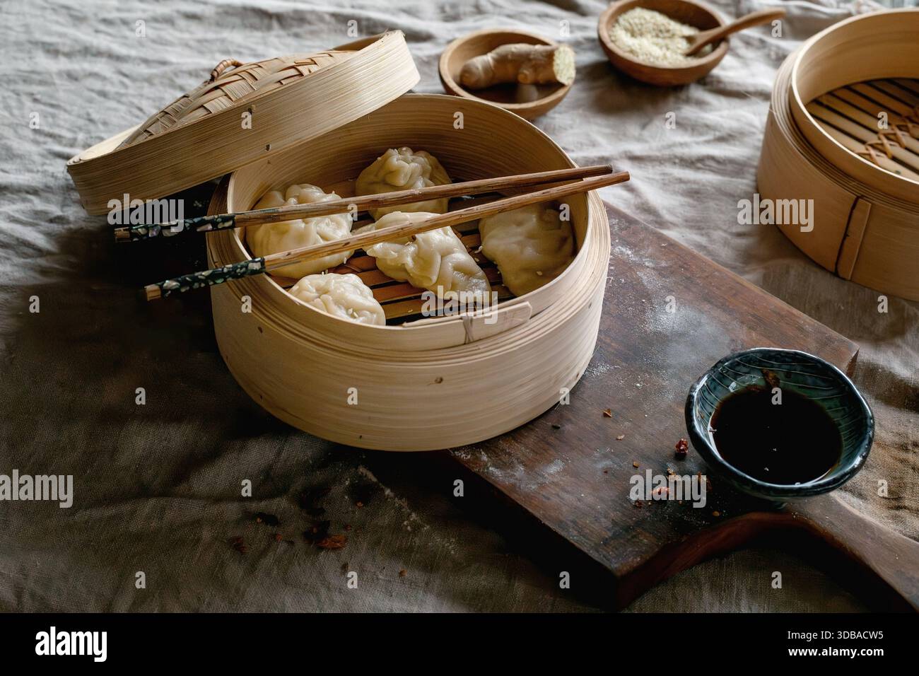 Bambusdampfer mit asiatischen gedämpften Knödeln, Essstäbchen, Sojasauce auf Holzbrett auf rustikalem Holztisch. Tageslicht. Asiatisches Essen Stockfoto
