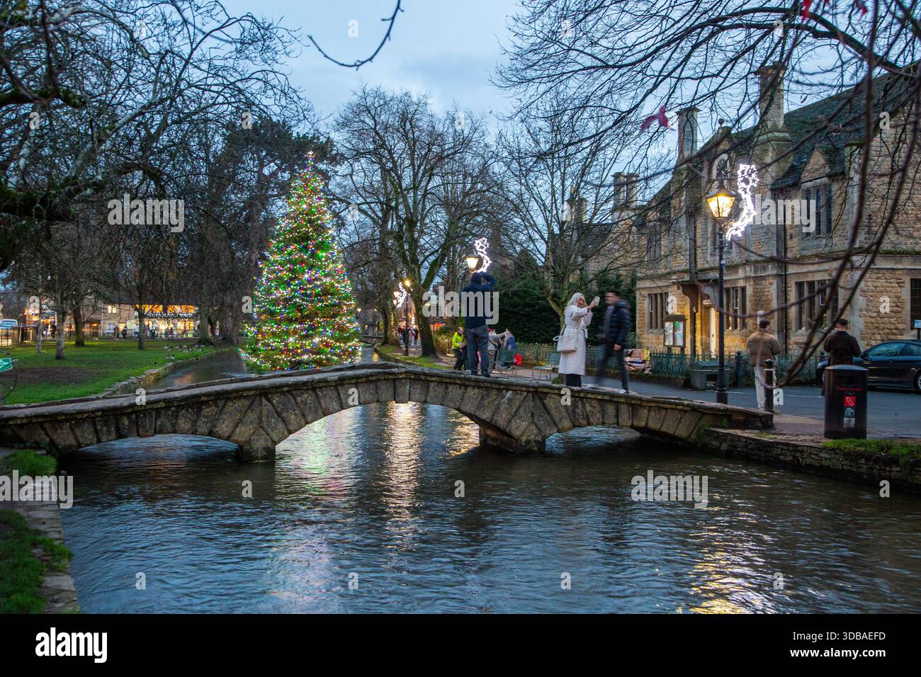 Schwimmender, geschmückter weihnachtsbaum mit Lichtern am Fluss Windrush, der durch das Dorf Bourton in Cotswold am Wasser Gloucestershire fließt Stockfoto