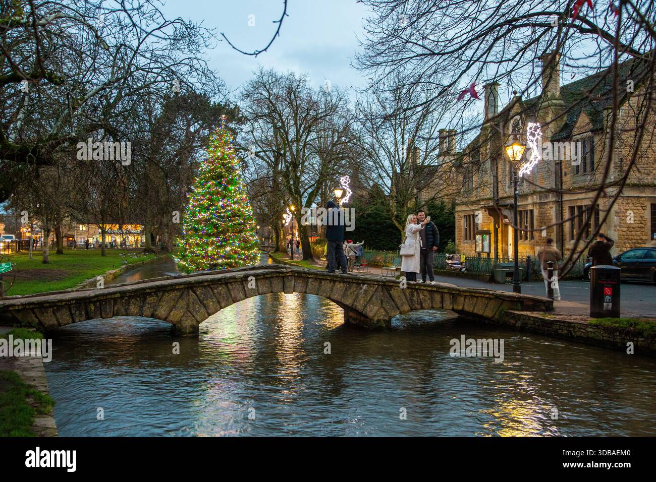 Schwimmender, geschmückter weihnachtsbaum mit Lichtern am Fluss Windrush, der durch das Dorf Bourton in Cotswold am Wasser Gloucestershire fließt Stockfoto