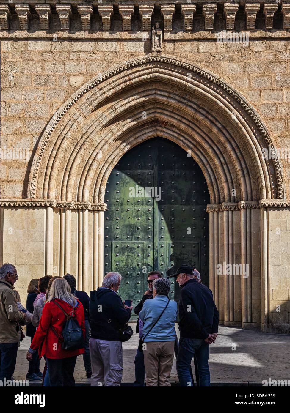 Eine Gruppe von Touristen steht in der Nähe des großen gotischen Portals der San Roman Kirche in Sevilla. Sie erkunden seine einzigartige Architektur und Geschichte. Stockfoto