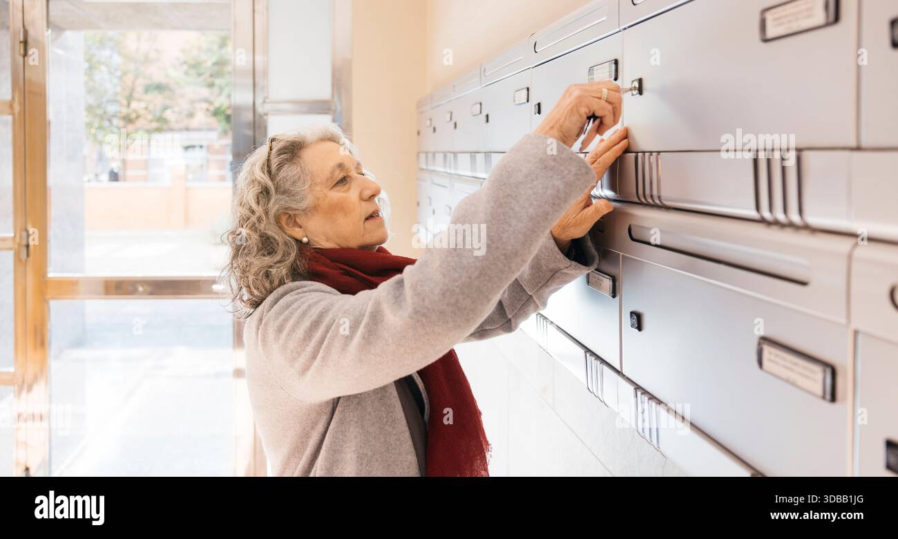 Ältere Frau, die den Schlüssel in einen gemeinschaftlichen Briefkasten einsteckte Stockfoto