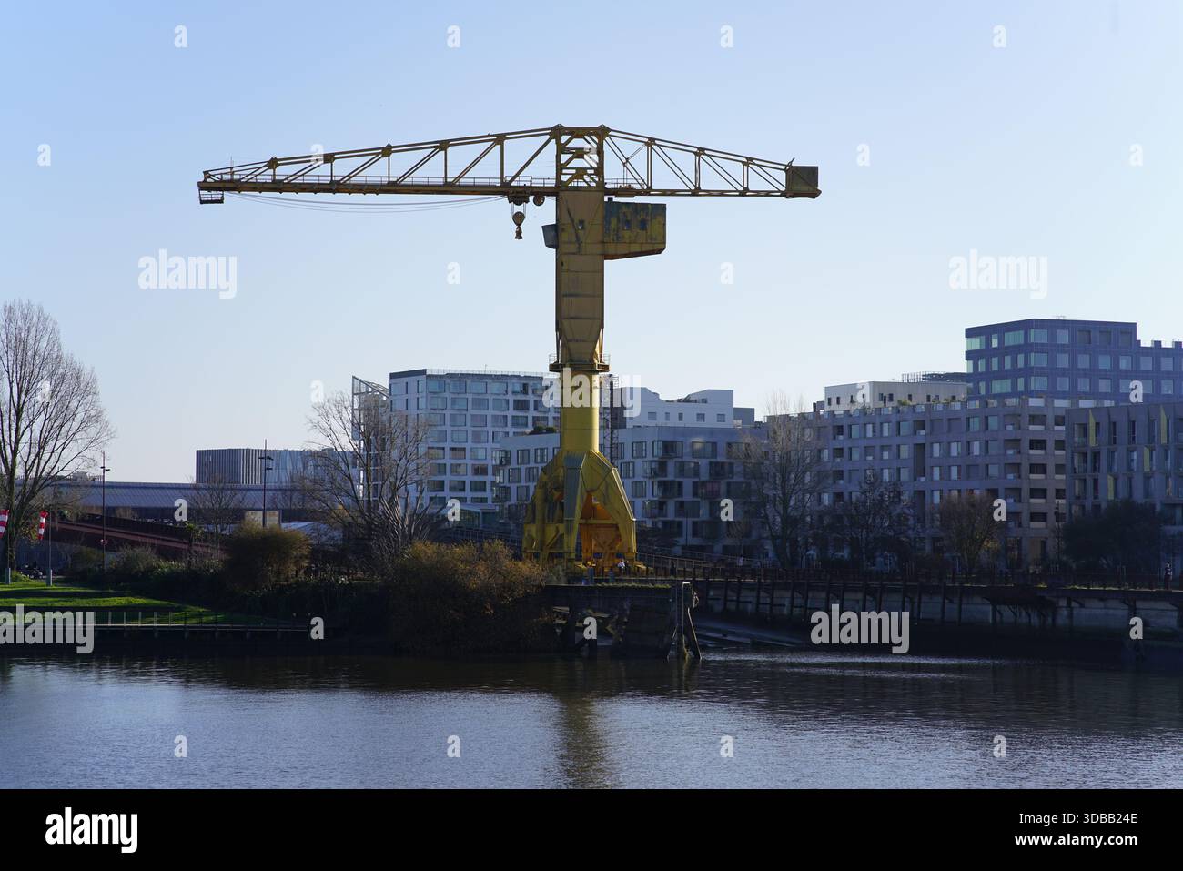 Ein hoher gelber Industriekran steht am Fluss mit modernen Wohnhäusern im Hintergrund. Nantes, Frankreich Stockfoto
