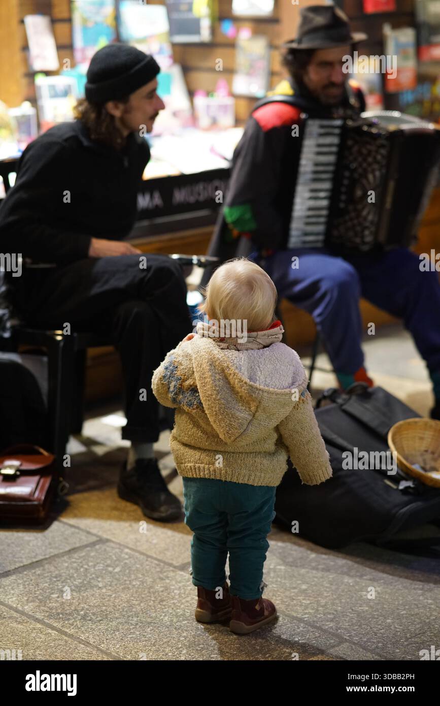 Ein kleines Kind, das zwei Straßenmusiker mit einem Akkordeon in einer Stadt beobachtet. Nantes, Frankreich Stockfoto