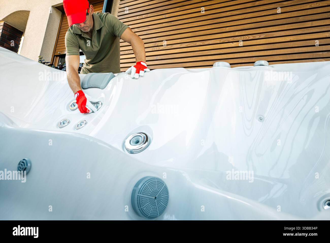Eine Person arbeitet tagsüber an der Reinigung eines Whirlpools außerhalb eines Hauses. Er benutzt Handschuhe und Werkzeuge, um sie zu pflegen. Stockfoto