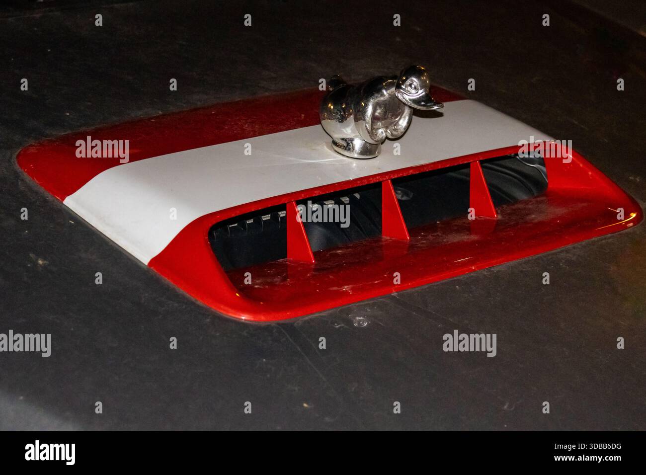 Nahaufnahme einer verchromten Kapuzendekoration, die wie ein Vogel geformt ist und auf der Motorhaube eines Autos montiert ist. Die Kapuze selbst ist in Rot und weiß gehalten. Das Bild ist ta Stockfoto