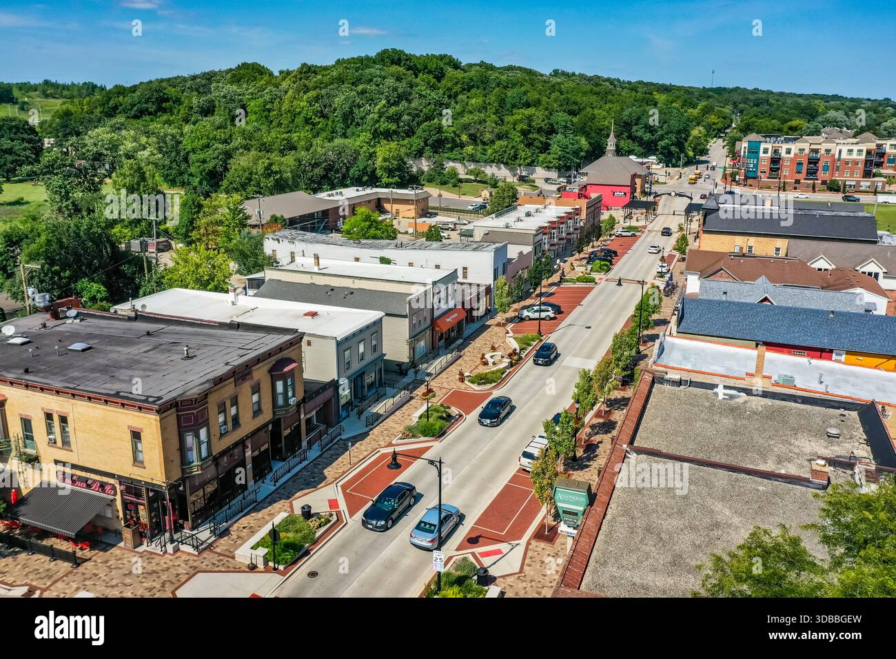 Blick aus der Vogelperspektive auf die Innenstadt von Algonquin, Illinois, mit historischen Gebäuden der Main Street, Verkehr, Gehwegen und üppigen grünen Hügeln an einem hellen Tag. Stockfoto