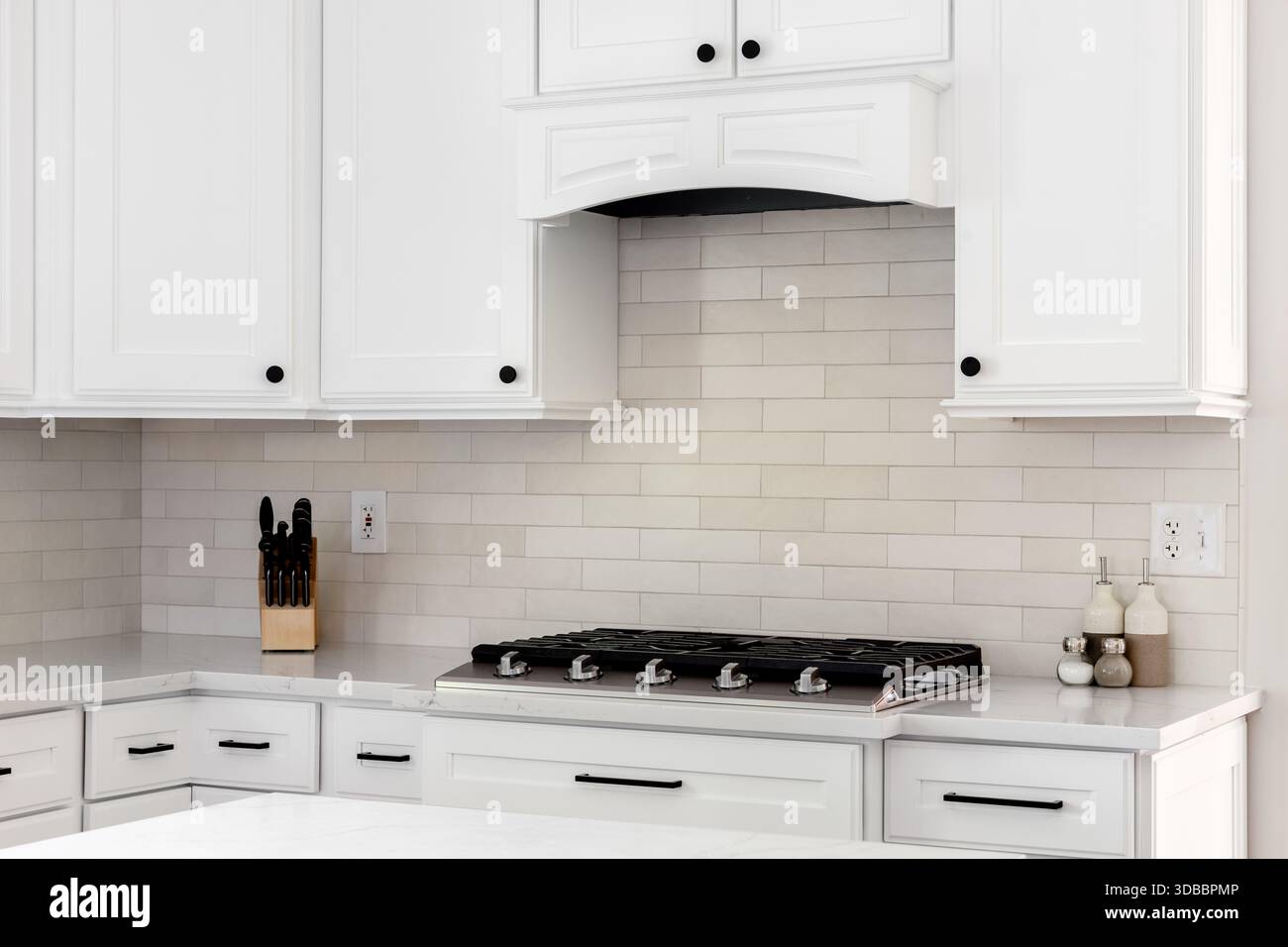 Ein Küchendetail mit weißen Schränken und Abzugshaube, braunen U-Bahn-Fliesen, Backsplash und einem Edelstahl-Kochfeld auf einer Marmorarbeitsfläche. Stockfoto