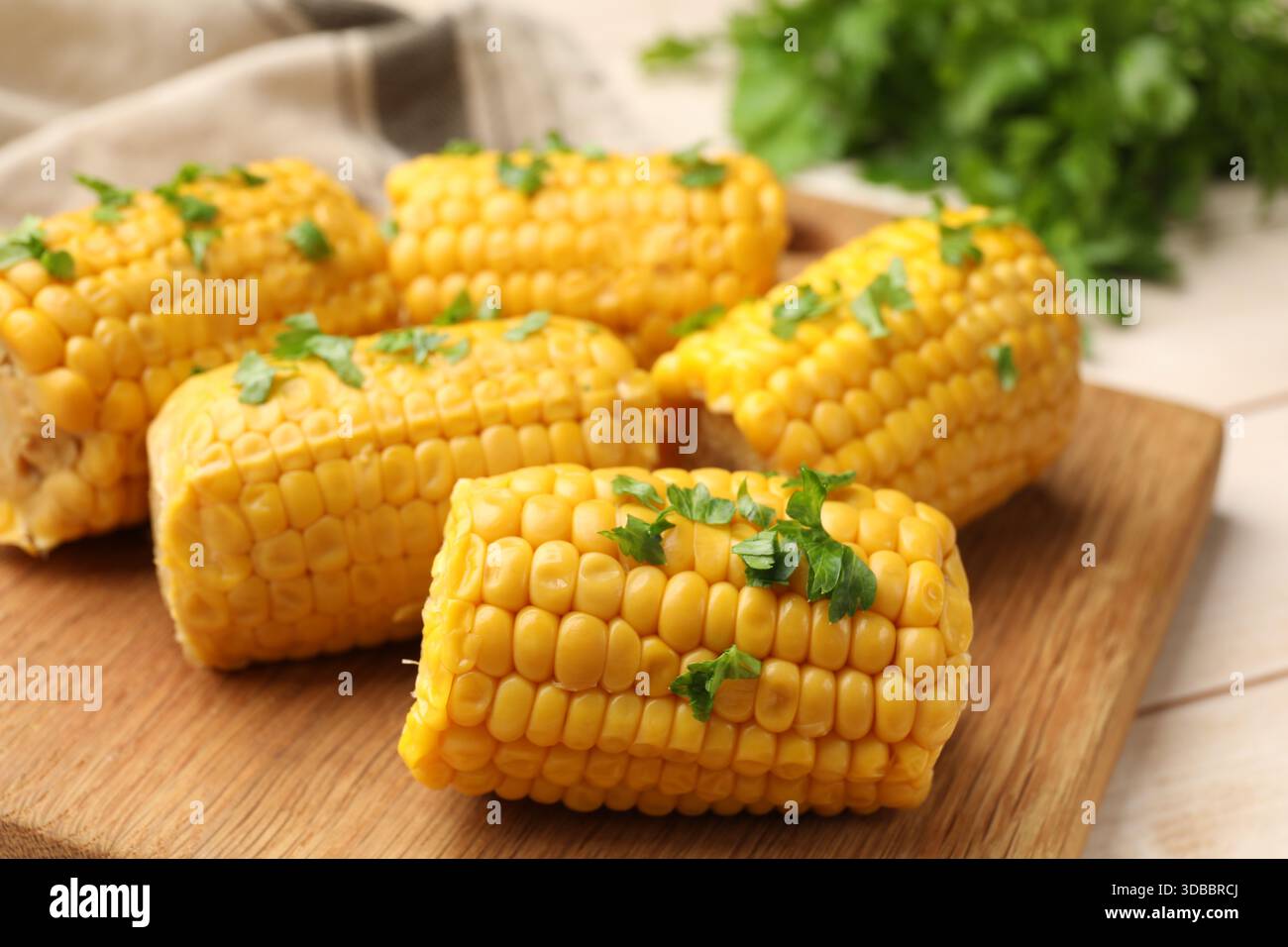 Stücke gekochter Maiskolben mit Petersilie auf Holztisch, Großaufnahme Stockfoto