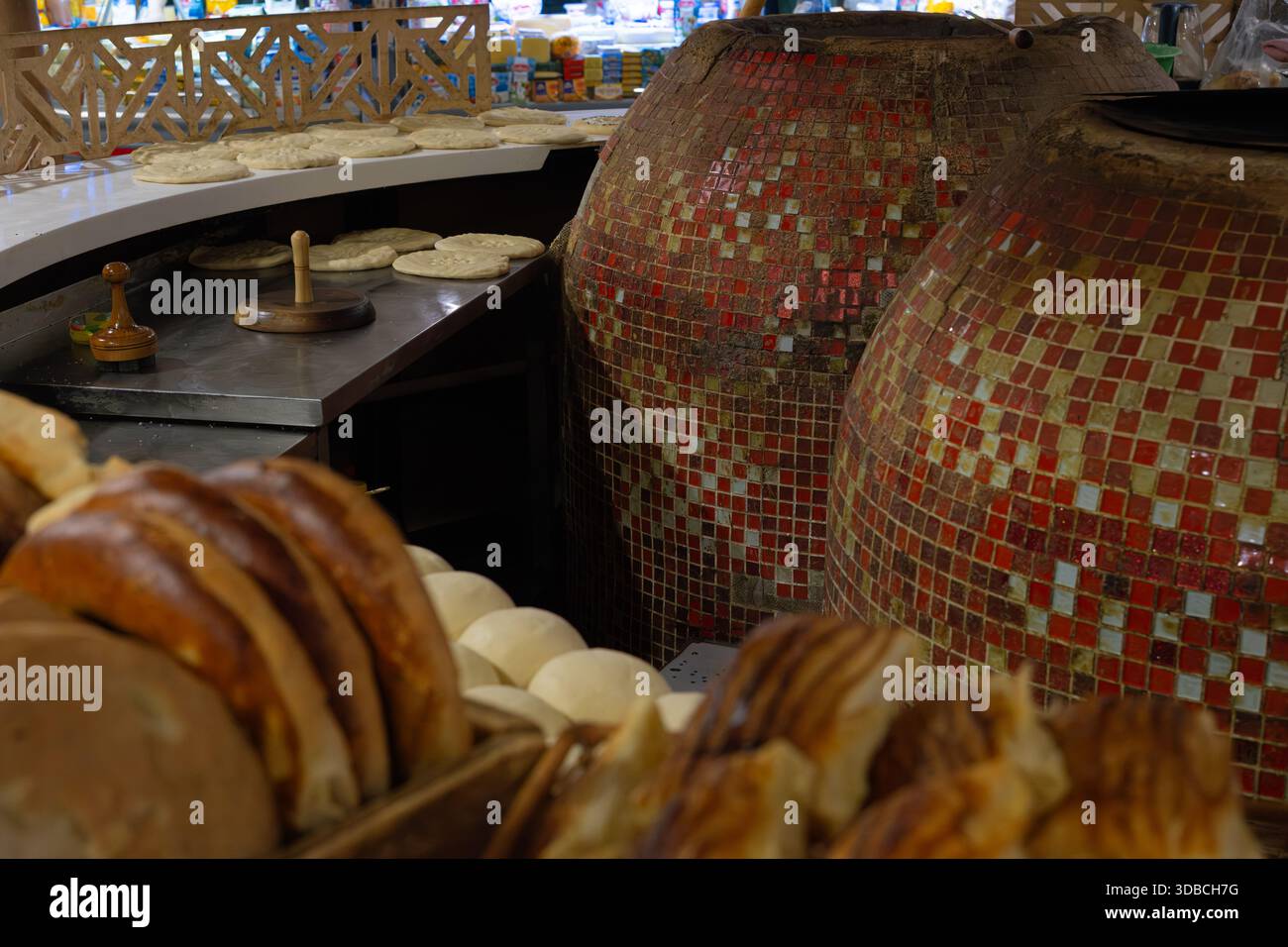 Traditionelle Bäckereiszene mit großen Tandooröfen zum Backen von Fladenbrot, frisch gerolltem Teig auf einer geschwungenen Theke und Holzwerkzeugen. Stockfoto