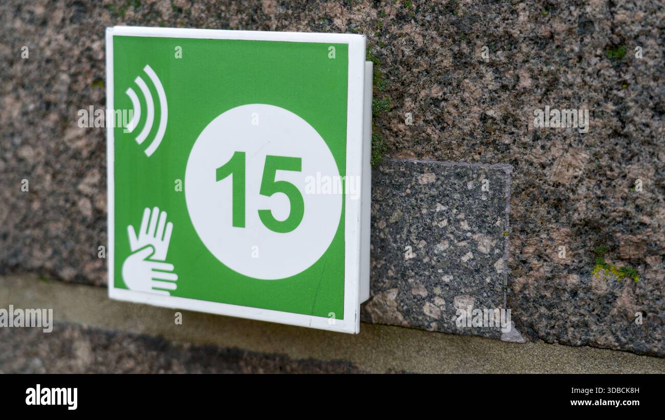 Ein quadratisches grünes Schild mit der Zahl 15 und einem Handsymbol auf einer grauen Steinoberfläche, das einen Halt oder einen Point of Interest für den Audioguide anzeigt. Stockfoto