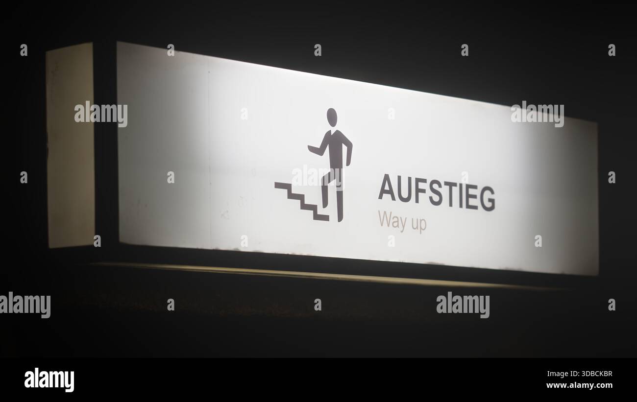 Ein beleuchtetes Schild mit einem Aufstiegssymbol und einer Treppe mit der Aufschrift „Aufstieg, Way up“, das eine klare Führung in einer dunklen Umgebung bietet. Stockfoto