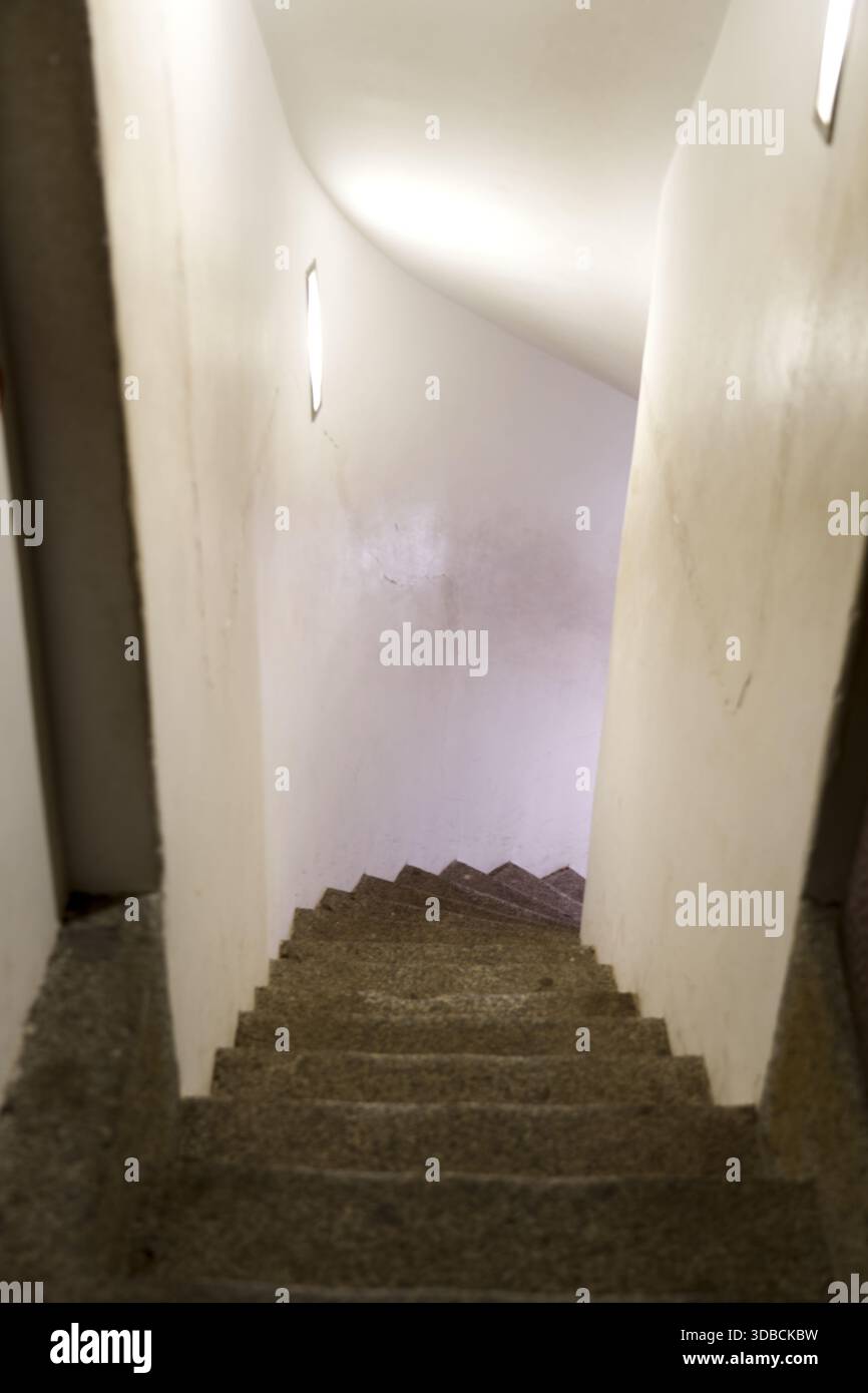 Eine schmale, geschwungene Treppe mit beleuchteten Wänden im Inneren eines Gebäudes, die ein fließendes und modernes architektonisches Element schafft. Stockfoto