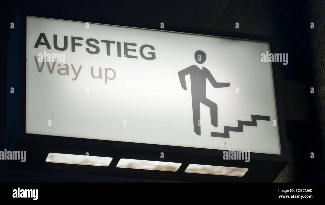 Ein beleuchtetes Schild mit einem Aufstiegssymbol und einer Treppe mit der Aufschrift „Aufstieg, Way up“, das eine klare Führung in einer dunklen Umgebung bietet. Stockfoto