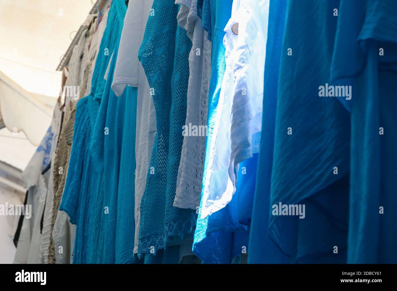 Blaue Textilien hängen vor Geschäften entlang einer Marktstraße in der Altstadt von Rhodos, Griechenland. Stockfoto